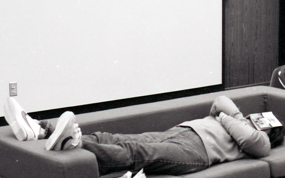 Student laying on couch with book on face