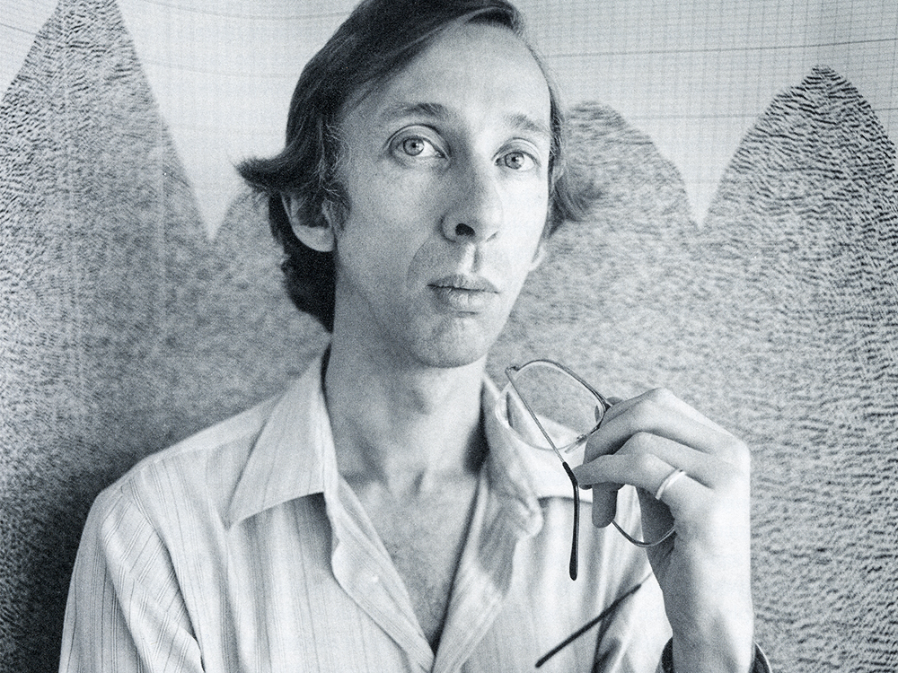 Black-and-white photo of George McMechan posing while holding his glasses