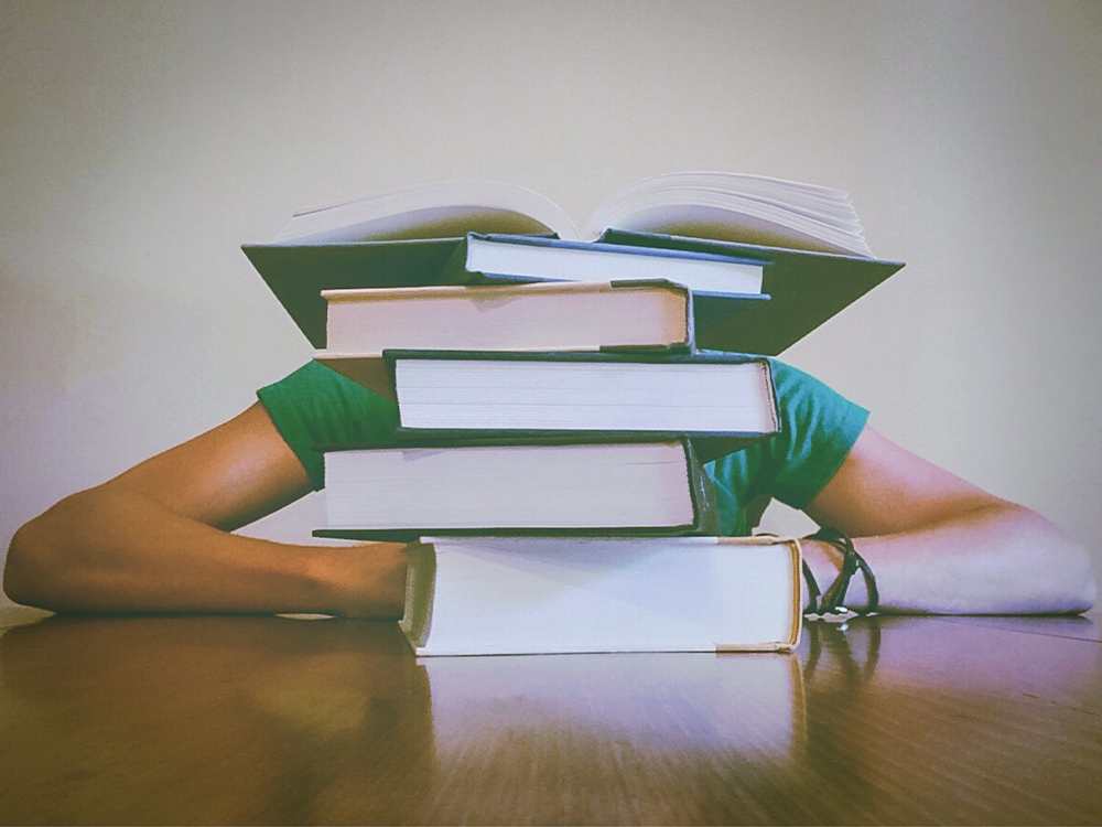 Person burying head behind a stack of books