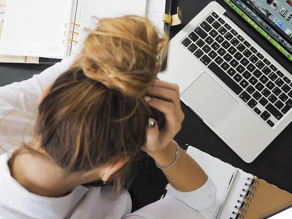 Woman with hands in hair surrounded by work items